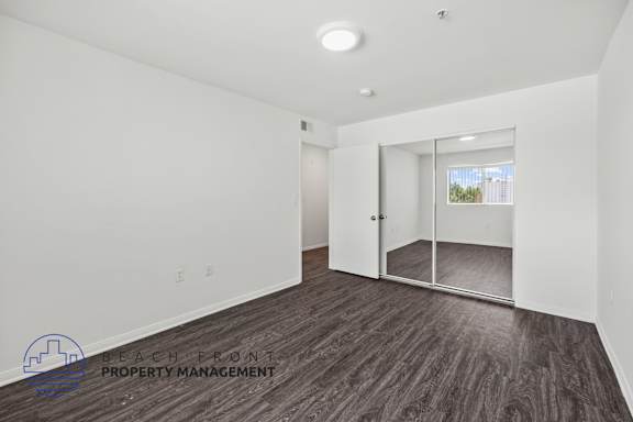 a bedroom with white walls and wood flooring and a mirrored closet