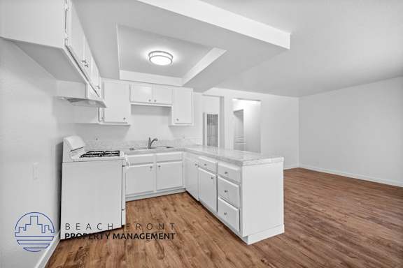 A white kitchen with wooden floors and a logo for Beachfront Property Management in the bottom left corner.