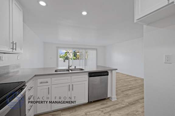 A kitchen with a sink and cabinets with a window in the background.