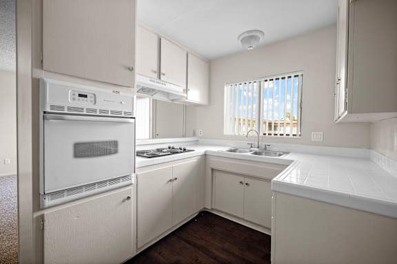 an empty kitchen with white cabinets and appliances and a window