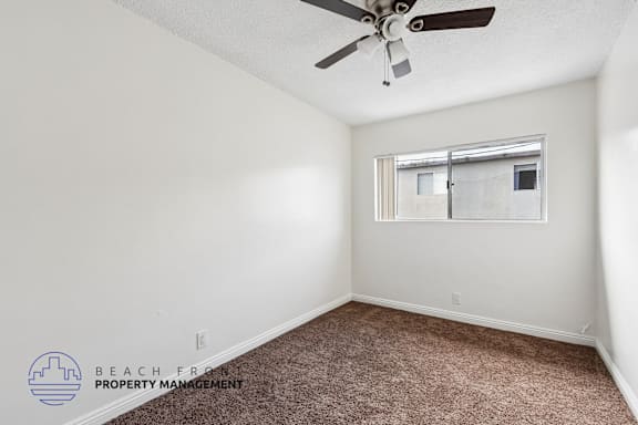 A room with a ceiling fan and a window with a view of a building outside.