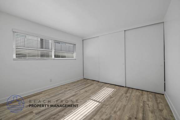 A room with a window and wooden flooring, with a logo for Beach Front Property Management.