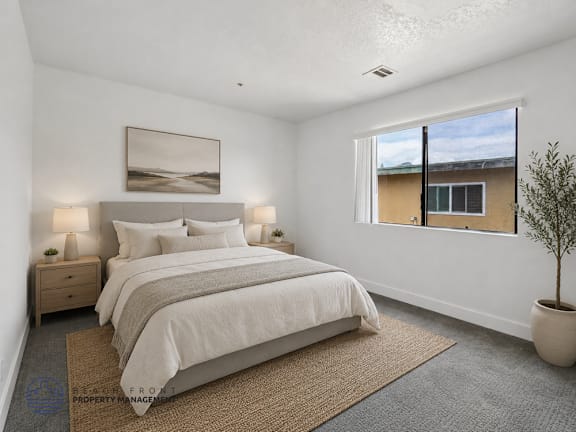 A bedroom with a large bed, a nightstand, a plant, and a framed picture on the wall.