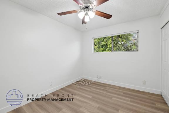 A room with a ceiling fan and a window with a view of trees.