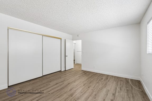 A room with white walls and wooden flooring, with a sliding door and a small white cabinet.
