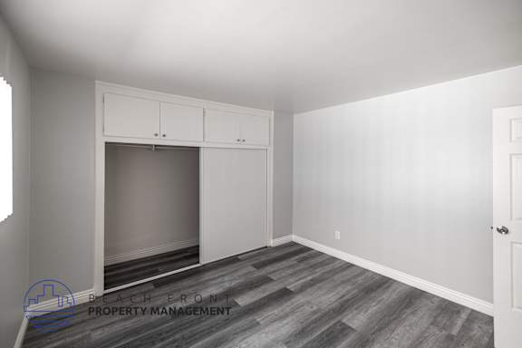 A room with a large window, a built-in cabinet, and a wooden floor.