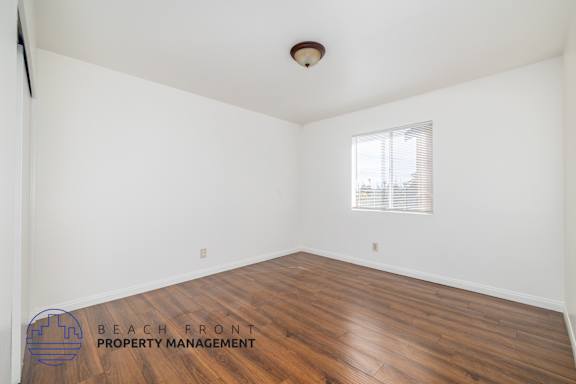 A room with wooden flooring and a window with blinds.