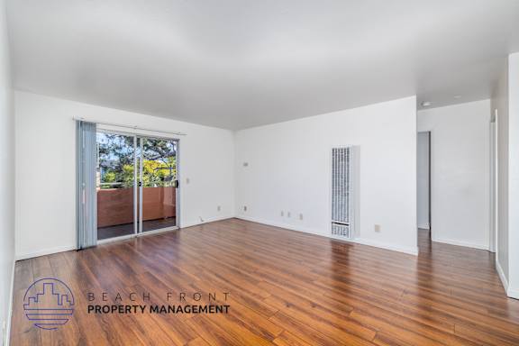 A spacious room with wooden floors and white walls, with a view of a balcony outside.