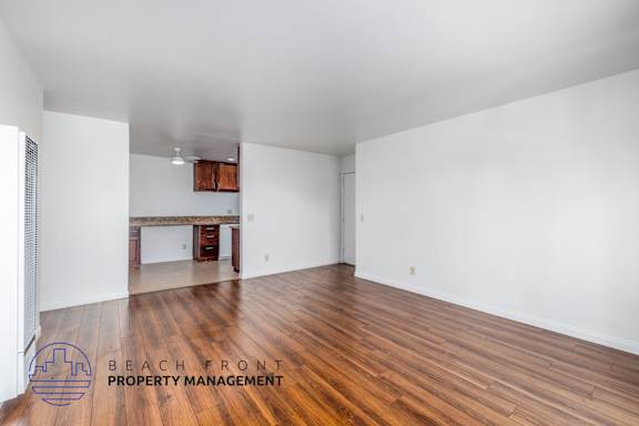 A spacious room with wooden flooring and white walls, with a logo for Beach Front Property Management in the bottom left corner.