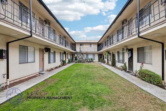 A row of apartment buildings with balconies and a lawn in the foreground.