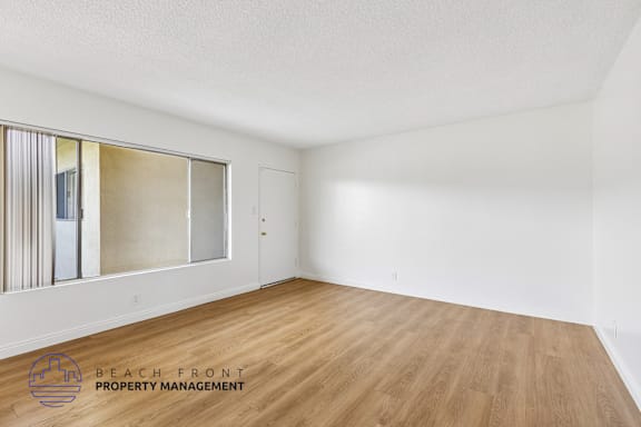 A room with wooden flooring and a large window with a view of the beach.