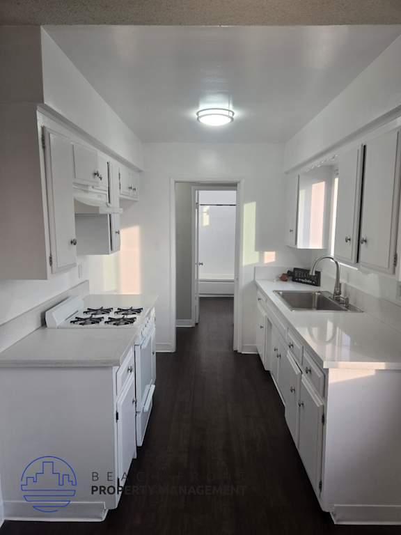 A clean, white kitchen with dark wood floors and a logo for Bel-Air Property Management in the bottom left corner.