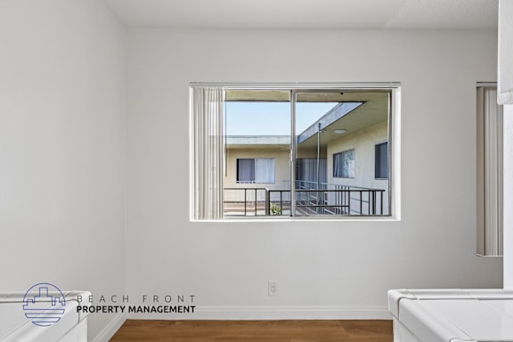 A room with a large window showing a balcony with chairs and a table.