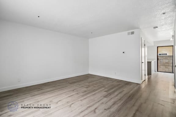 A spacious room with wooden flooring and white walls, with a door on the right side.