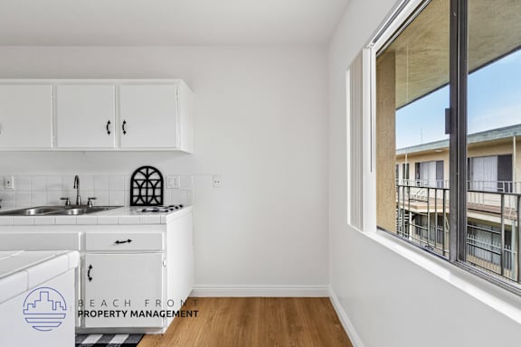 A kitchen with white cabinets and a window overlooking a balcony.
