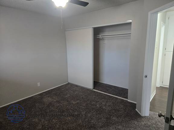 A room with a carpeted floor and a ceiling fan.