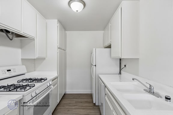 A white kitchen with a stove, sink, and cabinets.