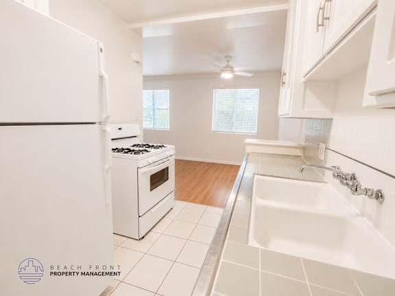 A white kitchen with a white fridge, stove, and sink.
