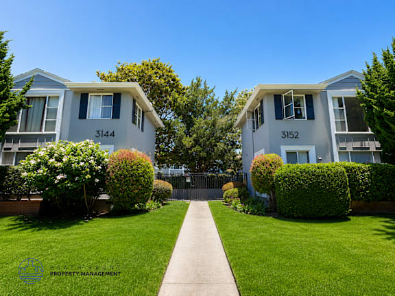 Two identical houses are located next to each other with a concrete pathway in between.