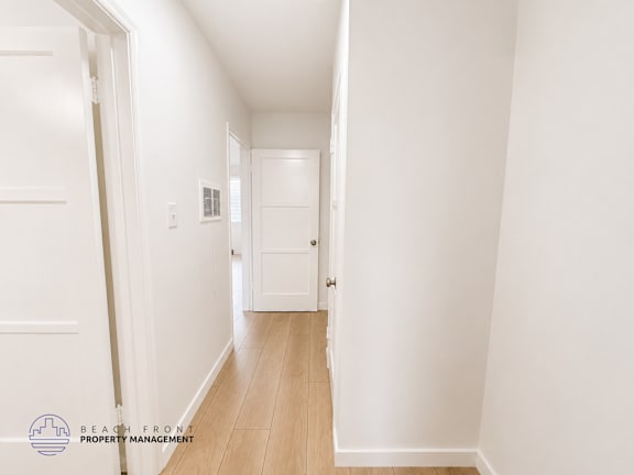 A hallway with white walls and wooden flooring.