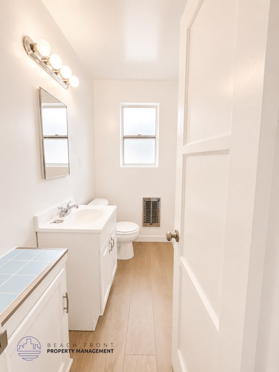 A small white bathroom with a toilet, sink, mirror and a window.