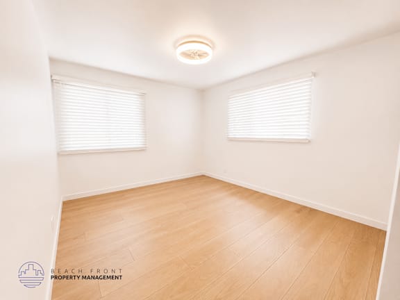 A room with wooden flooring and white walls, with a logo for Beach Front Property Management in the bottom left corner.
