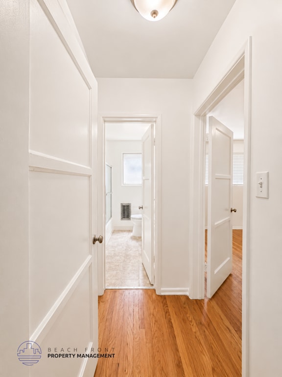 A hallway with white walls and wooden floors leading to a balcony.