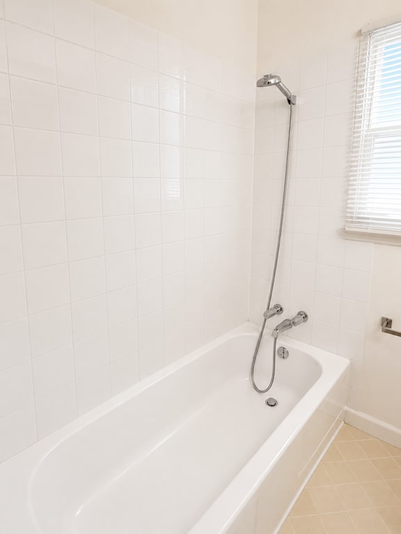 A white bathtub with a shower head and a window with blinds.