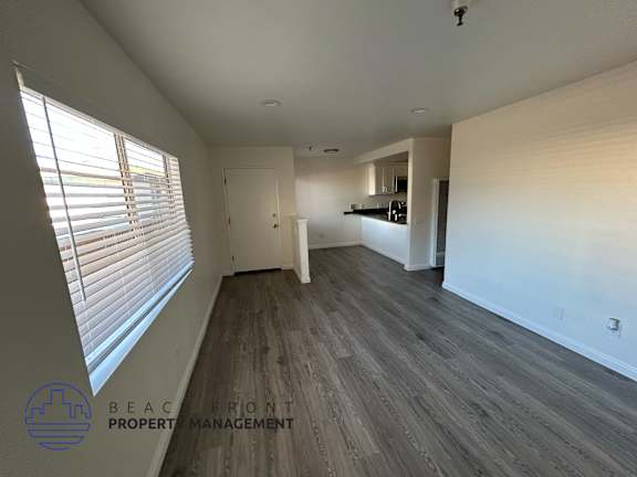 A spacious room with wooden flooring and white walls, with a logo for Beach Front Property Management in the bottom left corner.