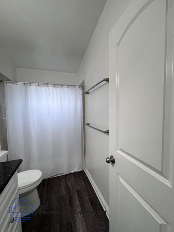 A white door is on the right of a bathroom with a toilet and a shower curtain.