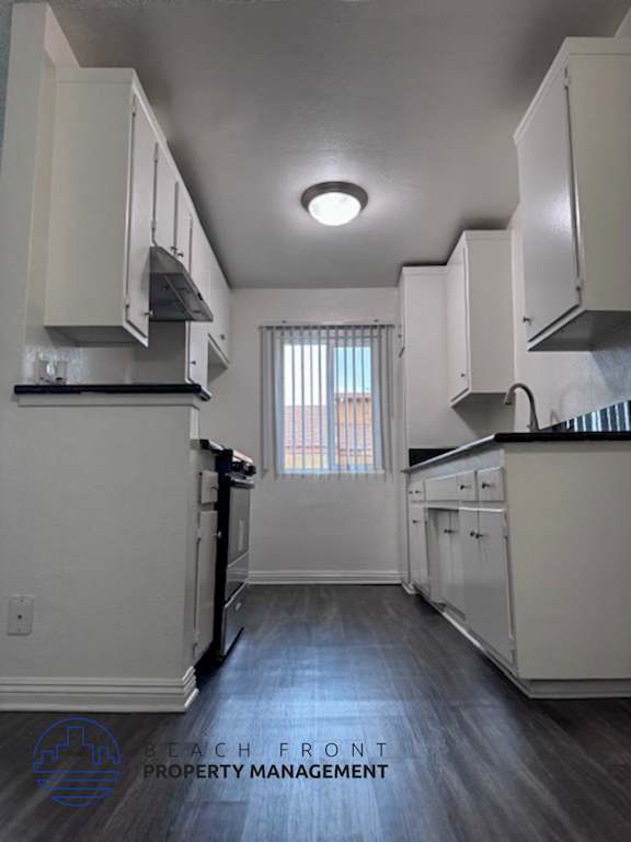 A kitchen with white cabinets and a window with blinds.