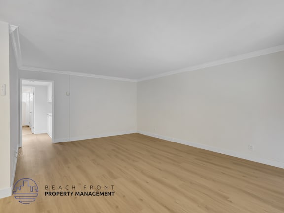 A room with wooden flooring and white walls, with a logo for Beach Front Property Management in the bottom left corner.