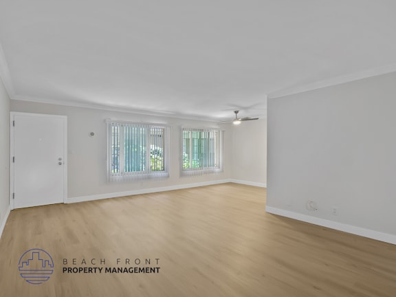 A spacious room with wooden flooring and a window with white curtains.