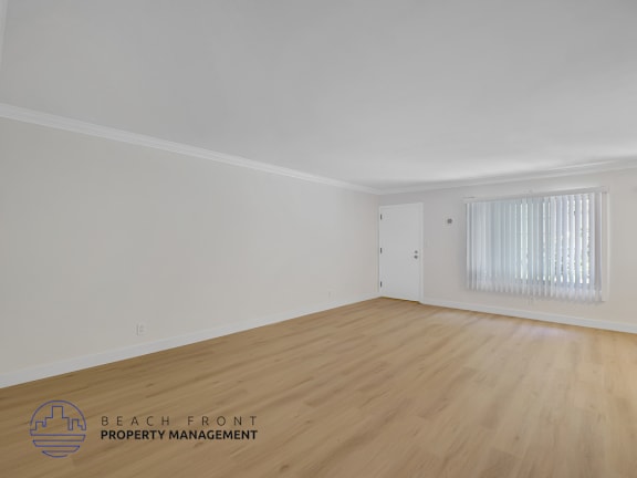 A room with wooden flooring and a window with white curtains.