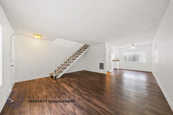 A spacious room with wooden floors and a staircase.