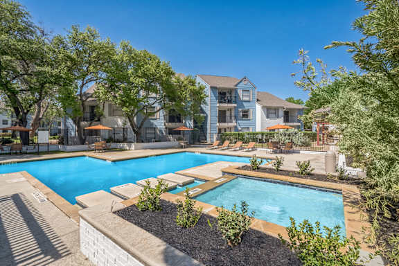 A swimming pool surrounded by trees and plants with a building in the background.