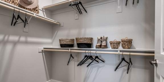 A white closet with clothes hanging and baskets on the shelf.