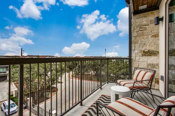 A balcony with two striped chairs and a table overlooks a parking lot.
