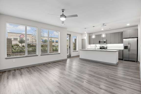 A spacious kitchen and living room with a ceiling fan and hardwood floors.