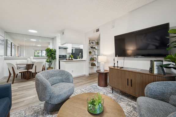 A living room with a grey armchair, a wooden coffee table, and a flat screen TV.