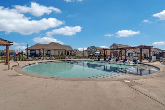 A large outdoor swimming pool surrounded by a fence and a pergola.