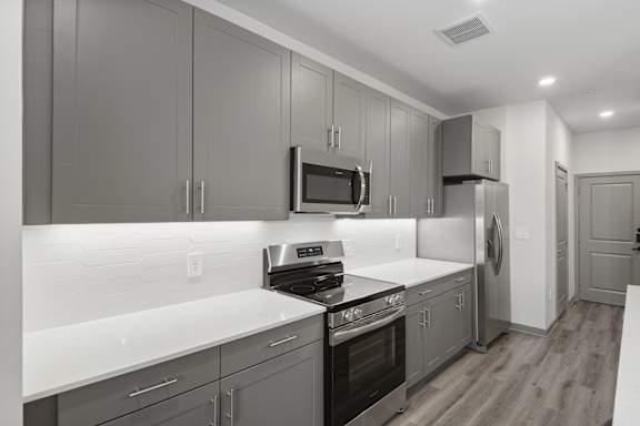 A modern kitchen with dark grey cabinets and white countertops.