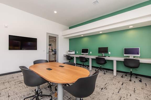 A conference room with a table surrounded by chairs and a green wall.