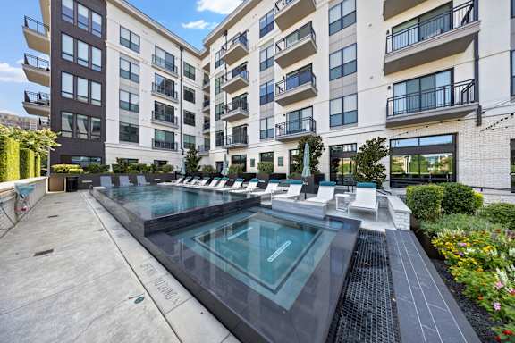 A large outdoor pool surrounded by lounge chairs and buildings.