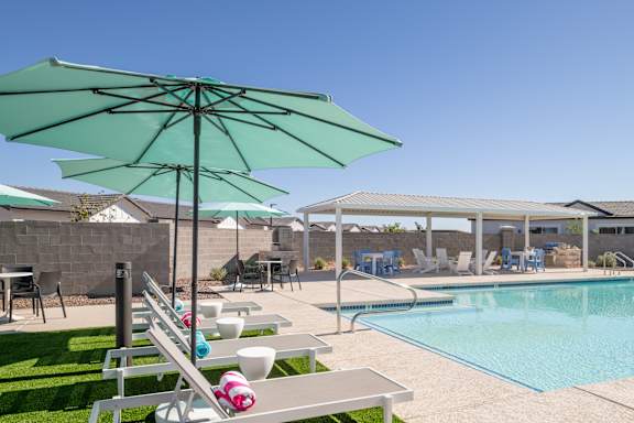 A poolside area with a green umbrella and a white bench.