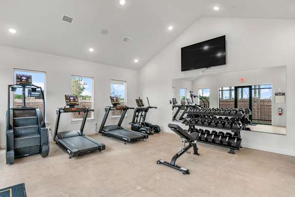 A spacious gym with treadmills, elliptical machines, and a bench press.