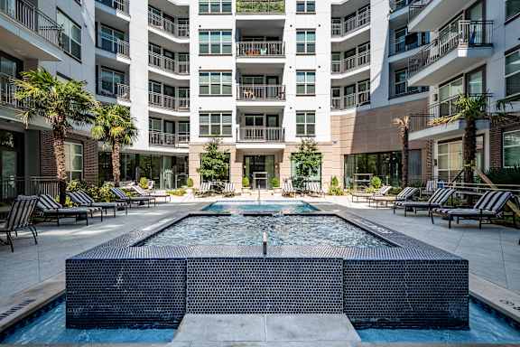 A large pool in the middle of a courtyard surrounded by lounge chairs and palm trees.