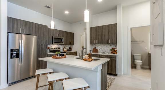A modern kitchen with a refrigerator, stove, and bar stools.