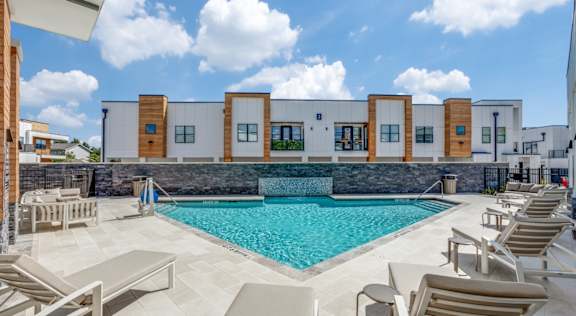 A swimming pool surrounded by lounge chairs in front of a building.