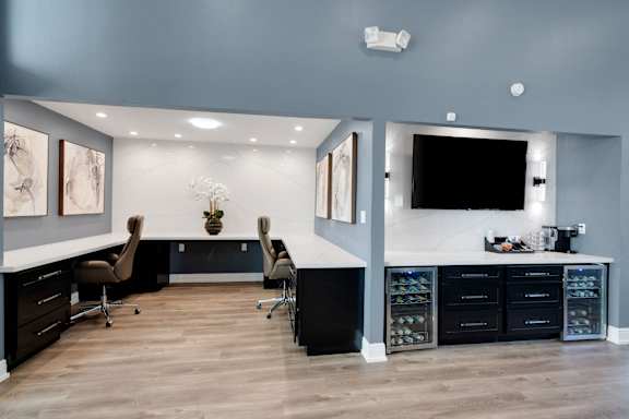 A modern home office with a desk, chairs, and a TV mounted on the wall.
